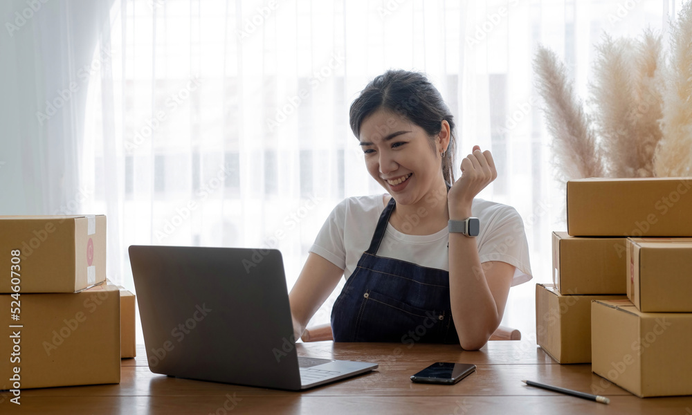 Startup SME small business entrepreneur of freelance Asian woman using a laptop with box Cheerful success Asian woman her hand lifts up online marketing packaging box and delivery SME idea concept Startup SME small business entrepreneur of freelance Asian woman using a laptop with box Cheerful success Asian woman her hand lifts up online marketing packaging box and delivery SME idea concept