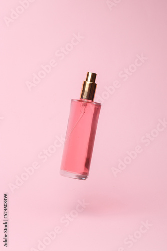 Perfume bottle with pink liquid flying in antigravity on pink background with shadow. Levitation object in the air. Beauty and fashion concept. creative minimalist layout