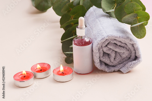Spa salon, beauty concert. Serum bottle with towel and sprig of eucalyptus and candle on beige background