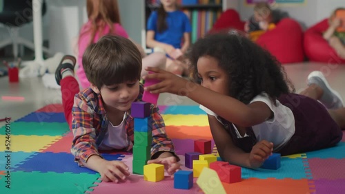 Cute multiethnic preschool kids playing with colored blocks on floor at nursery school