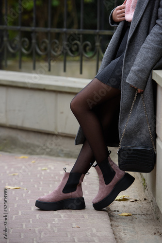 Fashionable and beautiful young woman, dressed in an pink knitted sweater, glasses, dark skirt and a gray classic trench coat and ankle boots