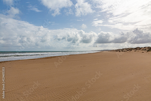 Evening view on small sand dune with green grass. Sandy beach at sea coast. Blue sky with white clouds. Sunset time