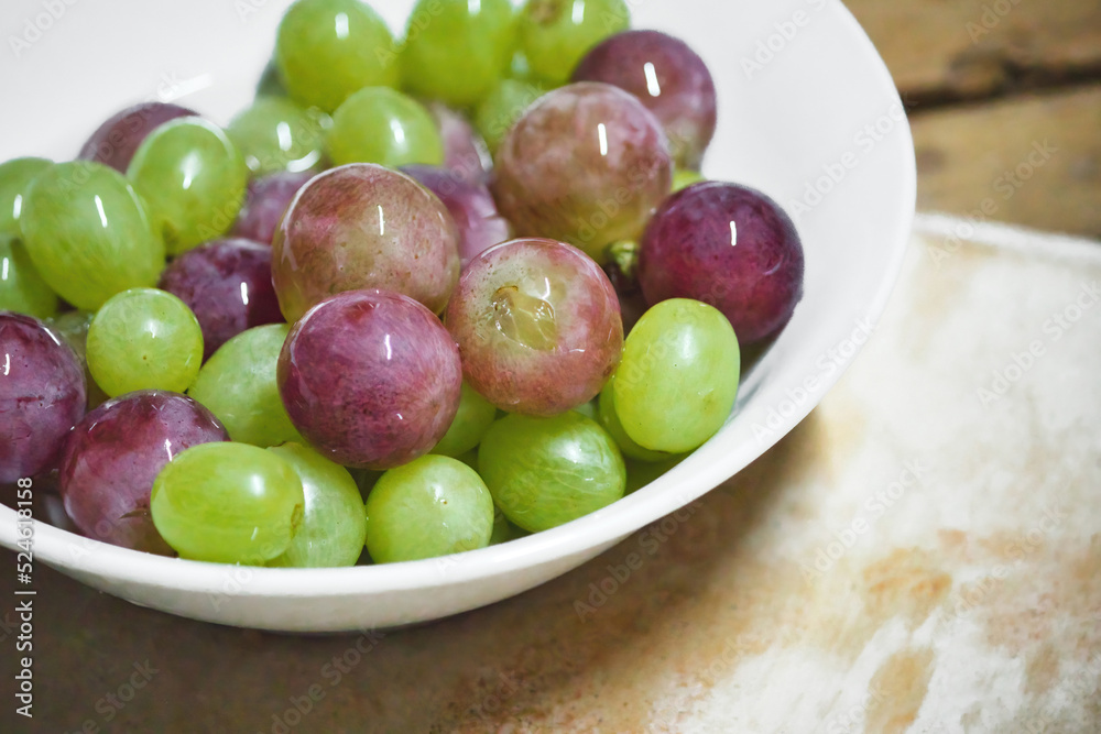 A white ceramic bowl full of green and purple or red unpeeled grapes A white ceramic bowl full of green and purple or red unpeeled grapes