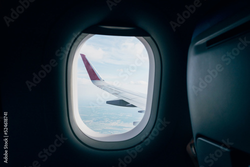 An airplane window with a view of an airplane wing and a city in the distance