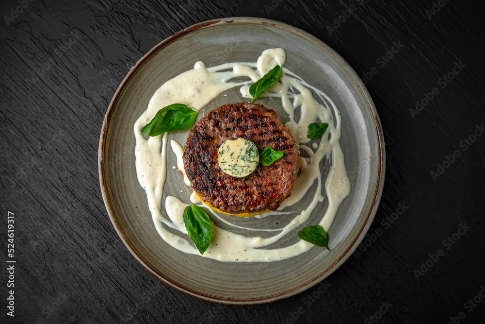 Beef steak or minced meat patty on a bed of mashed potatoes or sweet potatoes in a ceramic plate on a dark textured background. Restaurant menu Isolated on black