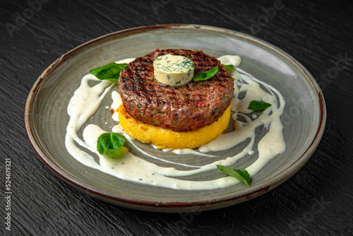 Beef steak or minced meat patty on a bed of mashed potatoes or sweet potatoes in a ceramic plate on a dark textured background. Restaurant menu Isolated on black