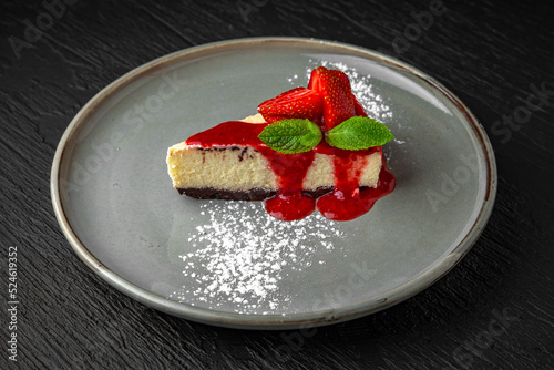 Dessert cheesecake with strawberries and mint in a ceramic plate on a dark textured background. Restaurant menu Isolated on black