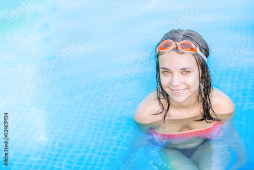 Happy teen girl wearing goggles enjoying in the pool at sunny day. Empty space for text