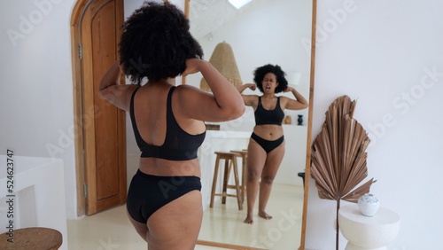 Acceptance of an Afro Asian woman of obesity. A black woman in front of a mirror in black lingerie looks at her magnificent forms and her body likes her. The concept of body positivity.