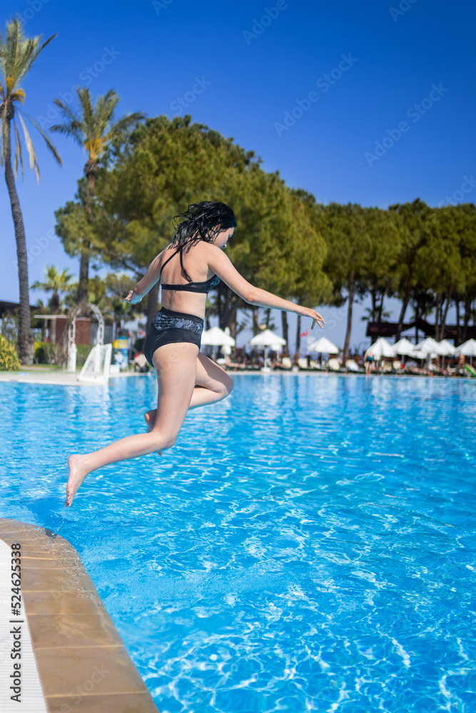 Young brunette teen girl jumping to a blue swimming pool in a hotel in Turkey. Having fun at vacation