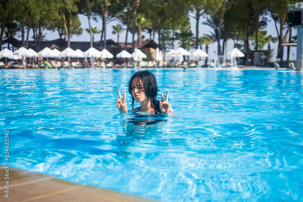 Young brunette teen girl posing in a blue swimming pool in a hotel in Turkey