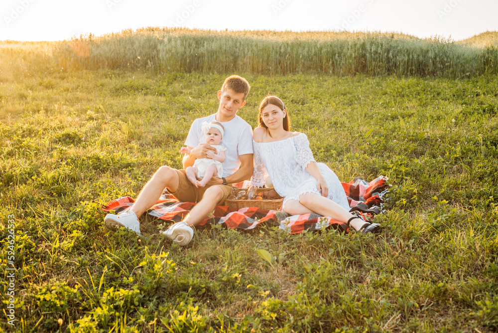Young family of three - mother, father and daughter having picnic outdoors during beautiful sunset. Slow living and happy family concept Young family of three - mother, father and daughter having picnic outdoors during beautiful sunset. Slow living and happy family concept