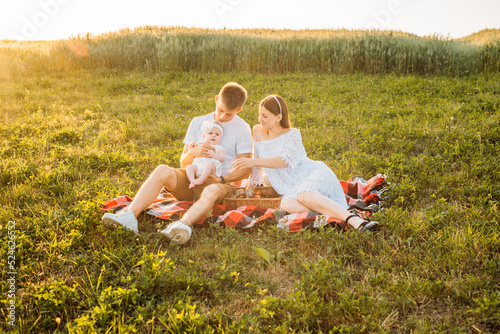 Young family of three - mother, father and daughter having picnic outdoors during beautiful sunset. Slow living and happy family concept