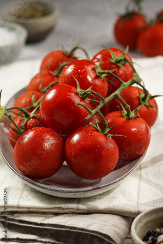 Fresh red tomatoes on branches on long oval plate on kitchen towels, grey background, close-up