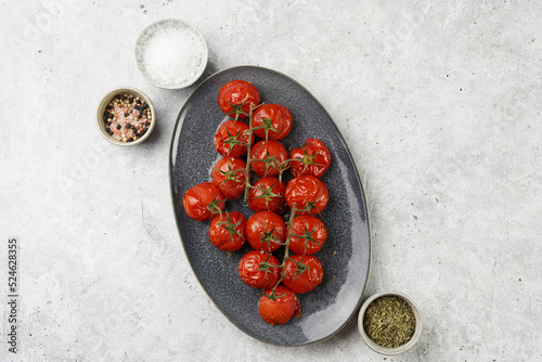 Roasted red tomatoes on branches on oval blue plate on grey background, top view, space for text