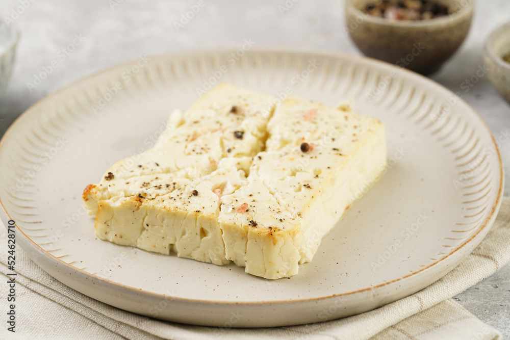oven baked sheep cheese feta with herbs, oil and spices on round off-white plate, kitchen napkins, grey background oven baked sheep cheese feta with herbs, oil and spices on round off-white plate, kitchen napkins, grey background