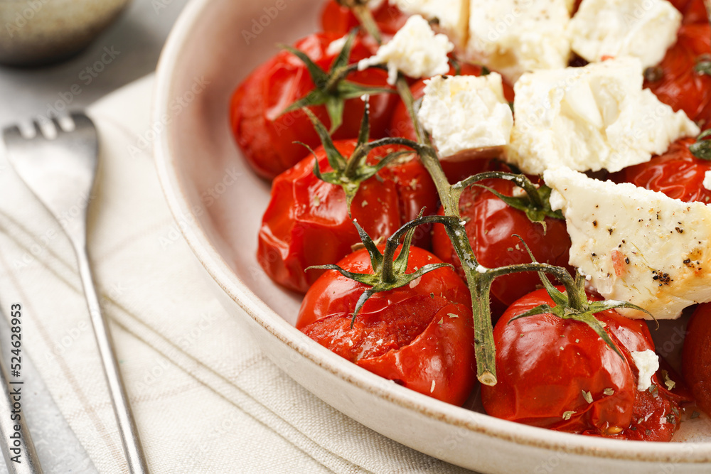 Roasted red tomatoes on branches with seasoned feta cheese on round off-white plate on kitchen napkins on grey background Roasted red tomatoes on branches with seasoned feta cheese on round off-white plate on kitchen napkins on grey background