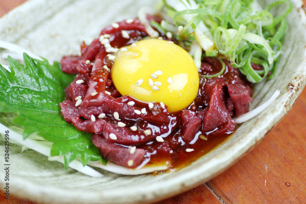 Obraz premium 鮮やかな赤身の馬肉に艶やかな卵黄と白ごまを添えた、鮮度抜群の馬肉ユッケ。とろけるような肉の質感と濃厚な旨みが際立つ一皿で、居酒屋の逸品メニューや馬肉料理専門店の販促に最適な高品質素材です。 | Fresh horse meat Yukhoe with raw egg yolk and green onions.