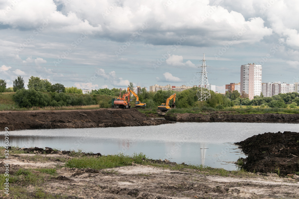 Fototapeta premium Crawler excavators dig the earth with a bucket. Drainage of swamps. Peat mining. Road construction works. Clearing the construction site.