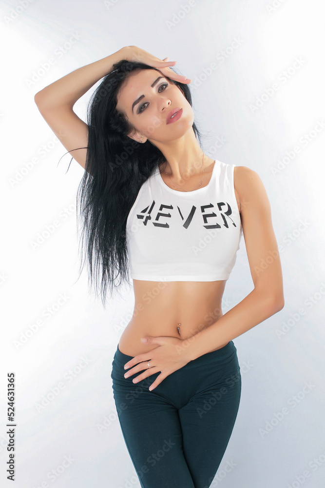 a pretty girl brunette stretching instructor, yoga, trainer, danser, posing in the studio on a white background in lasins and T-shirt a pretty girl brunette stretching instructor, yoga, trainer, danser, posing in the studio on a white background in lasins and T-shirt