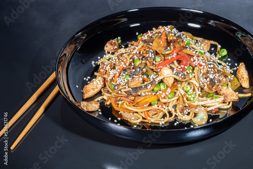 Udon noodles with meat, mushrooms and vegetables. Sprinkled with sesame seeds. Asian food, roast on black background,