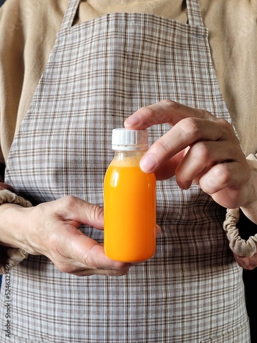 Person in rustic apron holding a bottle of orange juice in recycled plastic with copy space. A nutritious cocktail. The concept of healthy eating. Fitness drink. Energy drink after sports.