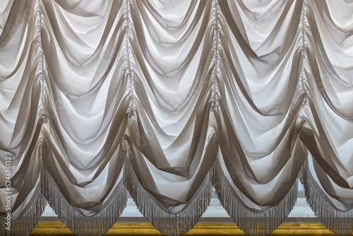 Background curtains made of thick white fabric with fringe. lambrequin. Interior design of the living room in a classic palace style.