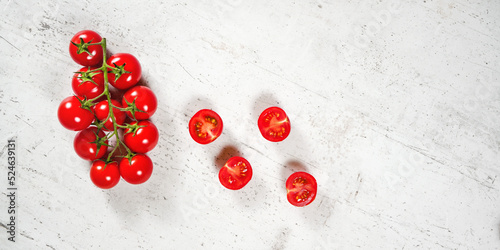 Vibrant small red tomatoes with green vines on white stone like board, view from above, empty space for text right side