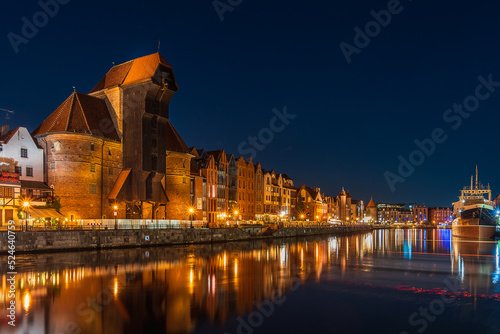 Night illumination of the embankment of the old town in Gdansk, Crane on Motława, reflections of lanterns of the embankment in the river Motława, Poland tourist attractions