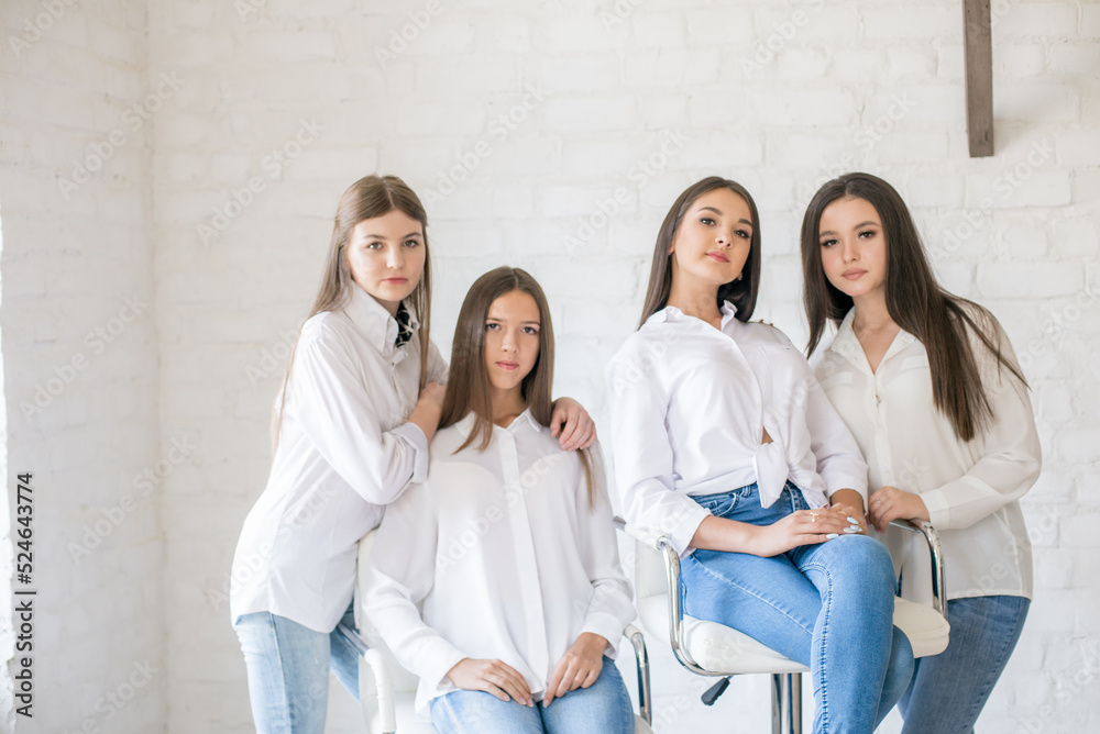 Fototapeta premium Pretty teenage girls models in trendy jeans and white shirts in the studio against the background of a white brick wall. Teenage fashion. beauty and fashion
