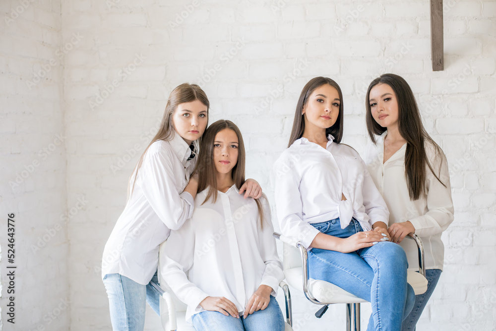 Fototapeta premium Pretty teenage girls models in trendy jeans and white shirts in the studio against the background of a white brick wall. Teenage fashion. beauty and fashion