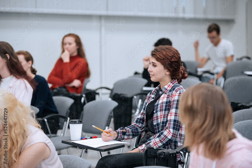 Several university students in casual clothes are sitting in the audience for a lecture and listening to the teacher