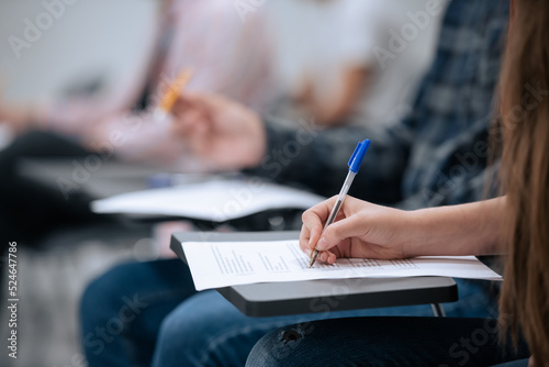 A close-up shot of a hand and a sheet of paper on which a student takes notes during a lecture at the university, without a face