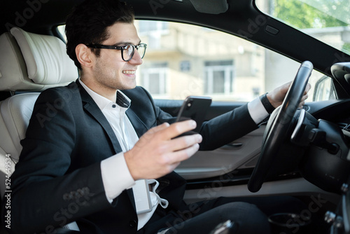 A male driver uses an app in his phone for a car, searches for a route in the navigator