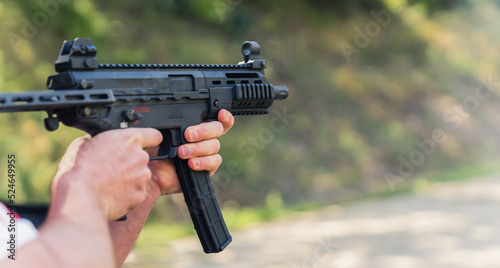 Hands holding submachine gun during training on shooting range. Blurred background. Outdoor horizontal shot. High quality photo