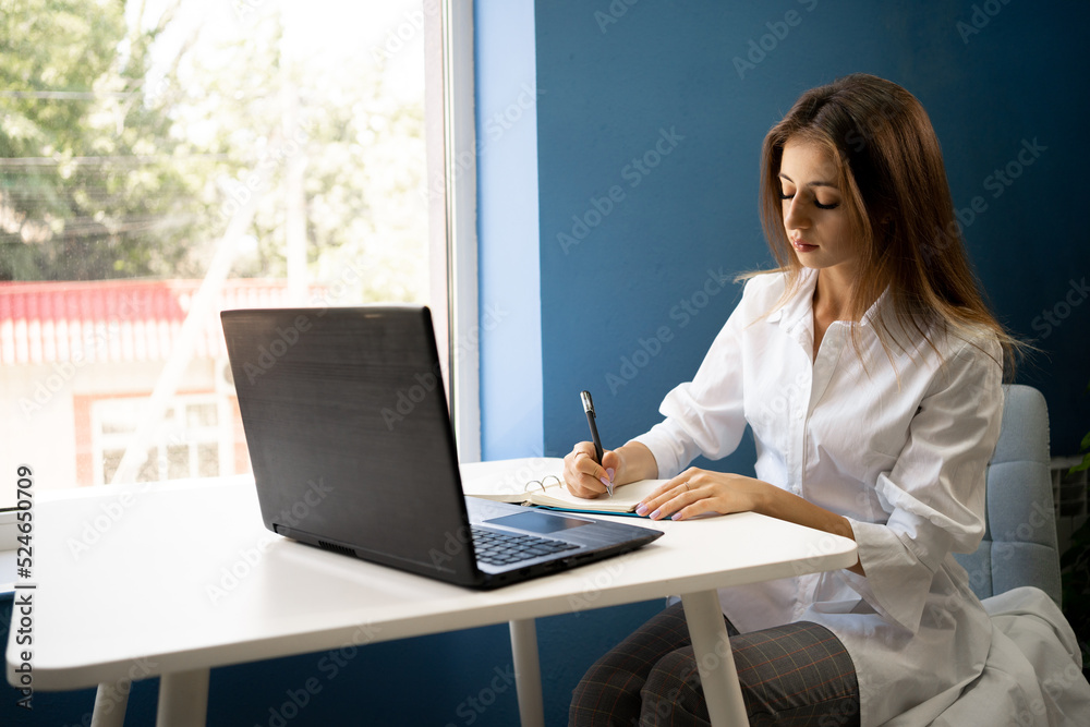 Young business woman sitting in cafe writing notes in notebook, freelancer working online using laptop, looking for job online at cafe Young business woman sitting in cafe writing notes in notebook, freelancer working online using laptop, looking for job online at cafe