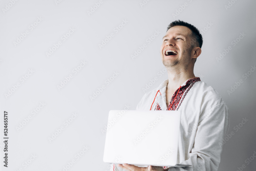 Guy in Ukrainian vyshyvanka is holding laptop and smiling. Guy in Ukrainian vyshyvanka is holding laptop and smiling.