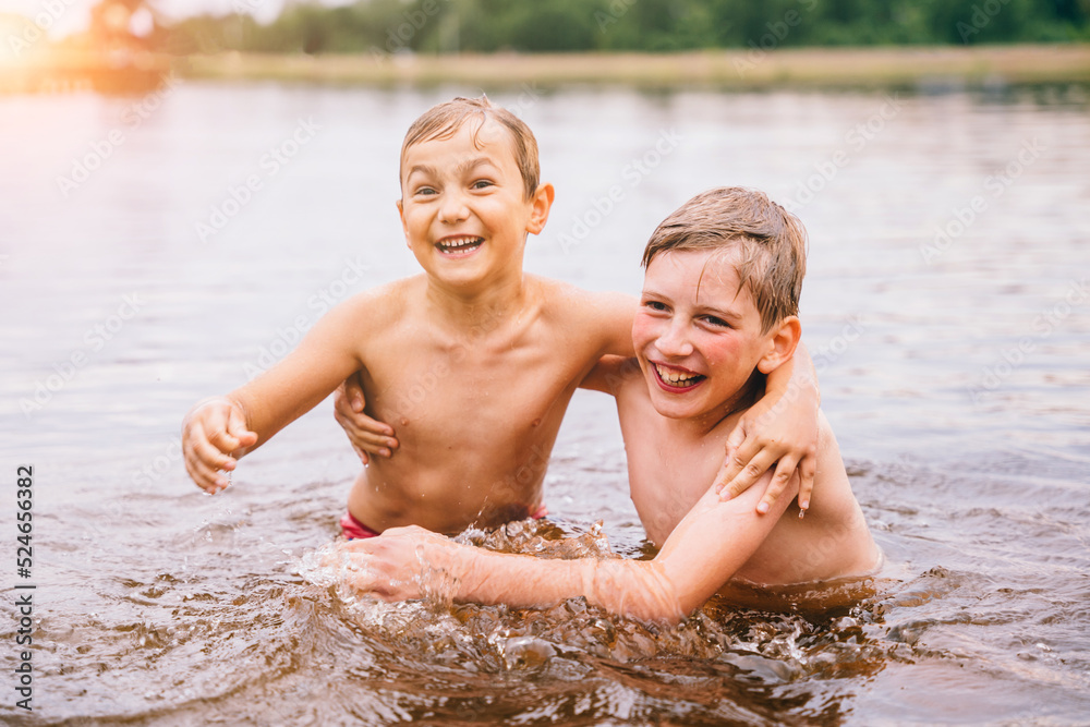 Emotional portrait of two cute happy wet school age boys inside the lake. Preteen boy swimming in lake. Summer cump, happy childhood, active lifestyle concept.