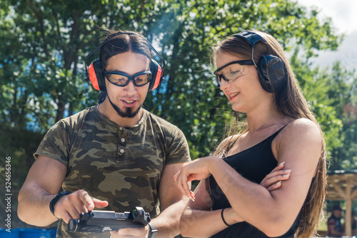 White man and woman wearing safety goggles and headphones talking about how to operate handgun. Firearms training at shooting range. Outdoor horizontal shot. High quality photo © PoppyPix