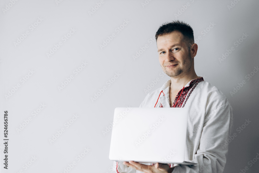 Guy in Ukrainian vyshyvanka is holding laptop and smiling. Guy in Ukrainian vyshyvanka is holding laptop and smiling.