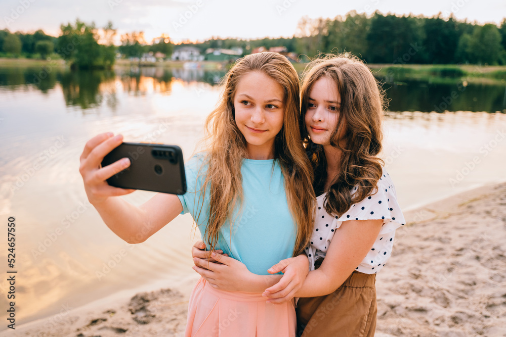 Vacation, relax, active lifestyle concept. Two teenager girls friends in eyeglasses having fun, laughing, taking selfie by smartphone at nature by the lake.