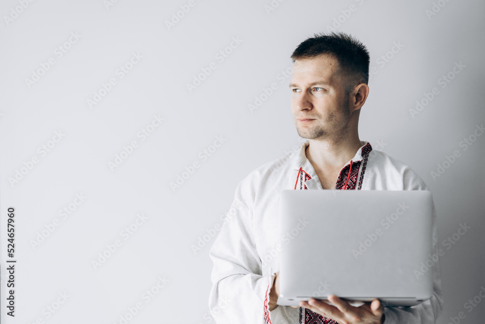 Guy in Ukrainian vyshyvanka stands holding laptop. Guy in Ukrainian vyshyvanka stands holding laptop.