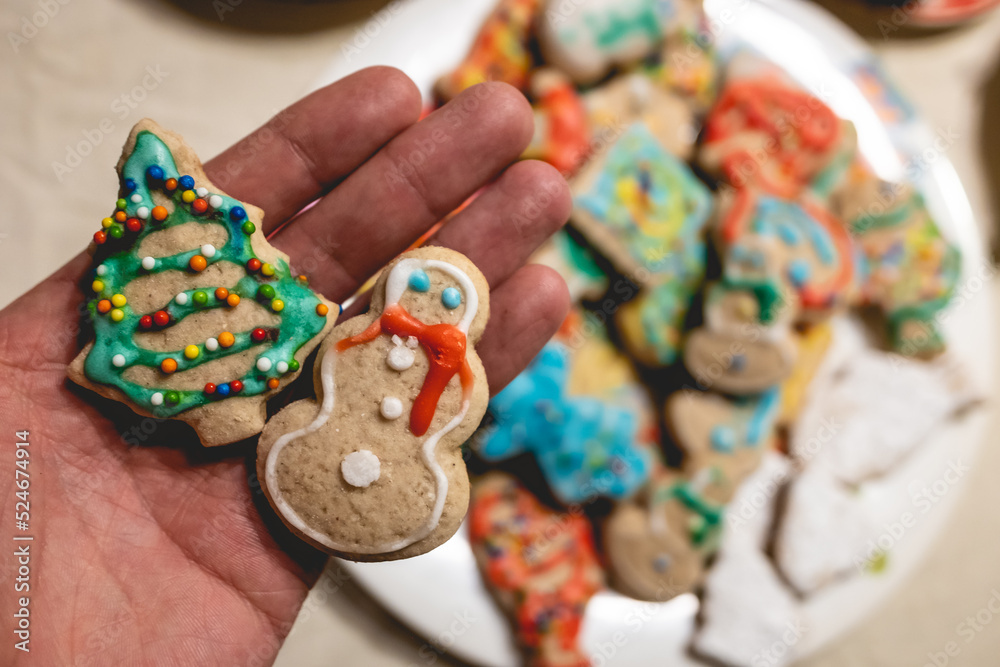 Hand holding a delicious and colorful handmade holiday cookies and plate with more cookies on a tea time table