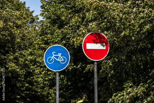 Bike path road sign and traffic ban sign on green tree leaves background