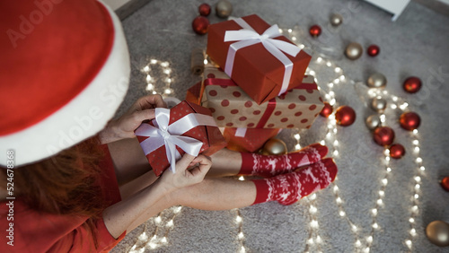 A young woman is packing Christmas presents for her friends and relatives. Girl creates New Year's packages with red paper, colored ribbons. Christmas decorations, preparation for the holiday season.