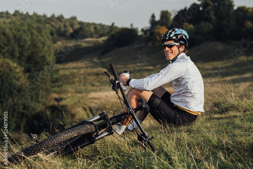 Professional Male Cyclist Drinking Water from Bottle, Man Sitting Near His Bicycle During His Journey Outdoors in Countryside