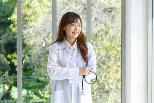 Beautiful and cheerful good mood young lady asian doctor dressed uniform smiling arm stethoscope on lobby hospital background..