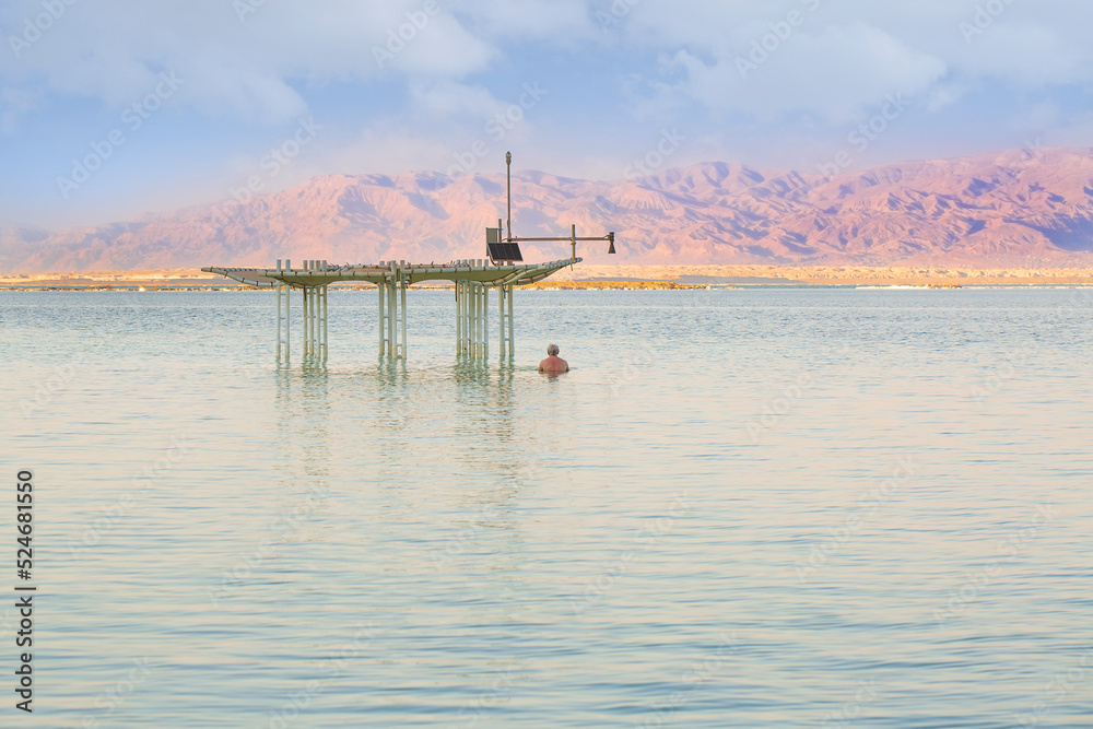 Sea season summer in Ein Bokek, Israel. Waterscape of seashore. Man floating in the waters of the Dead Sea, enjoying a moment of relaxation. Caucasian adult man is swimming at the beach of the resort