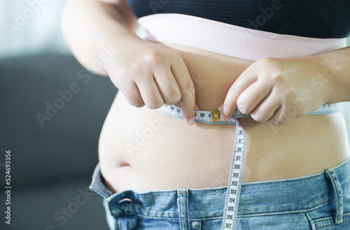 Obese Woman with fat belly in dieting concept. Overweight woman touching his fat belly and want to lose weight. Fat woman her waist with a centimeter..Shape up healthy stomach muscle 