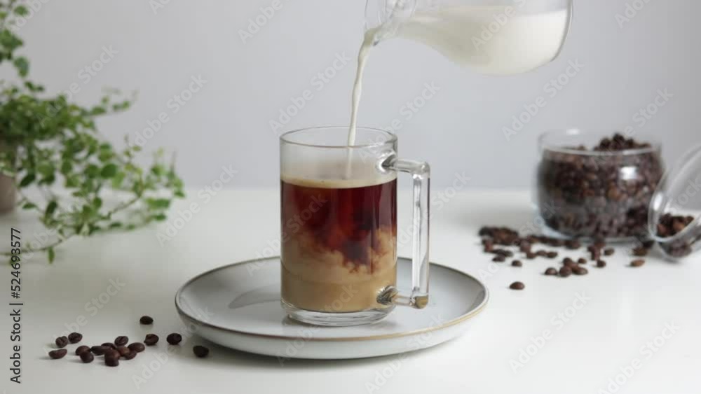 The process of pouring milk into coffee. A man pours milk into a glass of coffee. The process of pouring milk into coffee. A man pours milk into a glass of coffee.